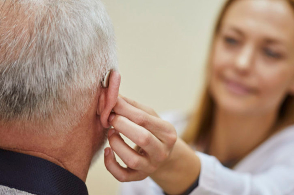 Female doctor applying hearing aid to senior man's ear